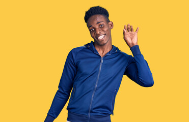 Young african american man wearing sportswear waiving saying hello happy and smiling, friendly welcome gesture