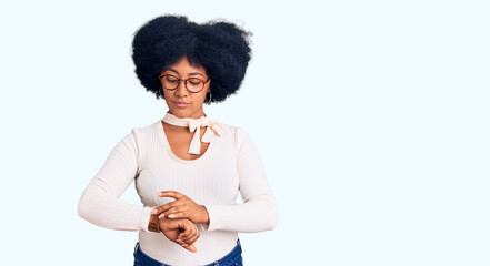Young african american girl wearing casual clothes and glasses checking the time on wrist watch,...