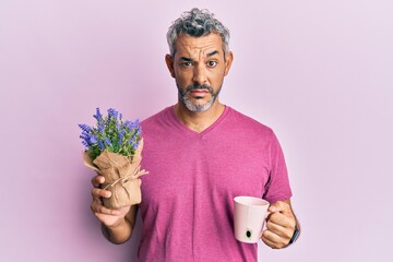 Middle age grey-haired man drinking a cup of infused lavender clueless and confused expression....