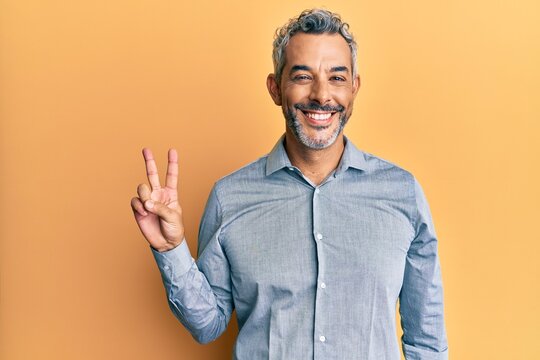 Middle age grey-haired man wearing casual clothes smiling with happy face winking at the camera doing victory sign. number two.