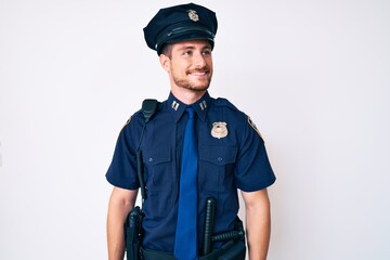 Young caucasian man wearing police uniform looking away to side with smile on face, natural expression. laughing confident.