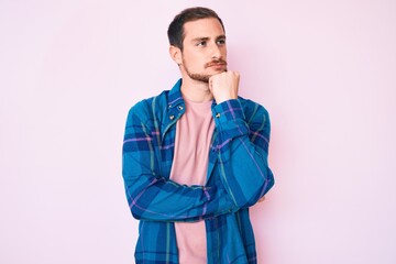 Young handsome man wearing casual clothes with hand on chin thinking about question, pensive expression. smiling and thoughtful face. doubt concept.