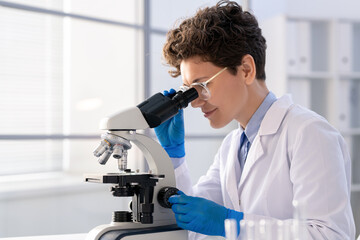Young woman looking in microscope while studying new chemical substances