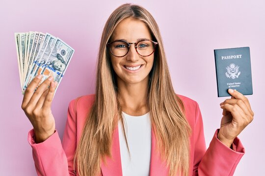 Young blonde woman wearing business style holding dollars and usa passport smiling with a happy and cool smile on face. showing teeth.