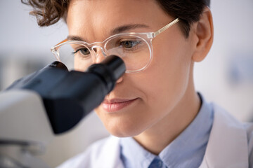 Head of young female scientist in eyeglasses and whitecoat working in laboratory