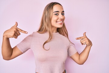 Young beautiful blonde woman wearing casual clothes looking confident with smile on face, pointing...