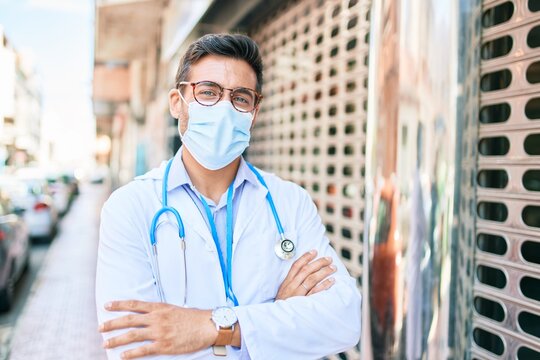 Young Handsome Hispanic Doctor Wearing Uniform And Coronavirus Protection Medical Mask Standing At Town Street.