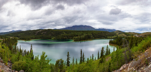 Fototapeta premium Panoramic Beautiful View of Emerald Lake during a cloudy summer day. Located near Whitehorse, Carcross, Yukon, Canada. Nature Background Panorama