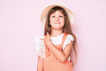 Little caucasian kid girl with long hair wearing spring hat smiling cheerful pointing with hand and finger up to the side