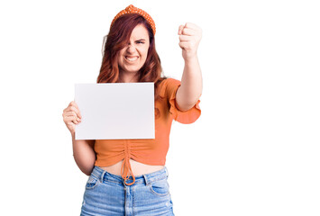 Young beautiful woman holding cardboard banner with blank space annoyed and frustrated shouting with anger, yelling crazy with anger and hand raised