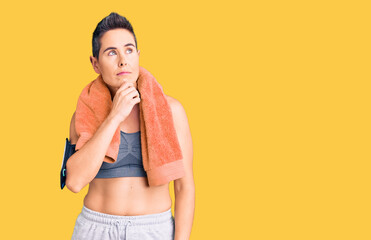 Young woman with short hair wearing sportswear and towel using smartphone with hand on chin thinking about question, pensive expression. smiling with thoughtful face. doubt concept.