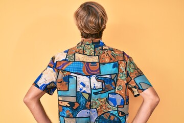 Young blond man wearing summer shirt standing backwards looking away with arms on body
