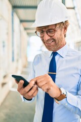 Business architect man wearing hardhat standing outdoors of a building project using smartphone