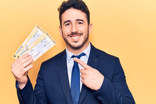 Young hispanic man wearing suit holding boarding pass smiling happy pointing with hand and finger