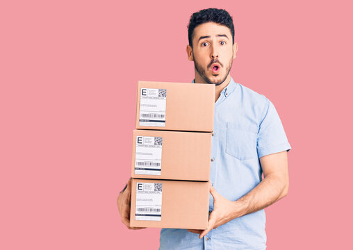 Young hispanic man holding delivery package scared and amazed with open mouth for surprise, disbelief face
