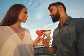 Low angle shot of young couple looking each other in the eyes, clinking wine glasses outdoors on sunset