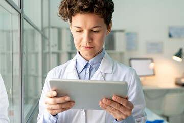 Young serious scientist or chemist in whitecoat looking through information