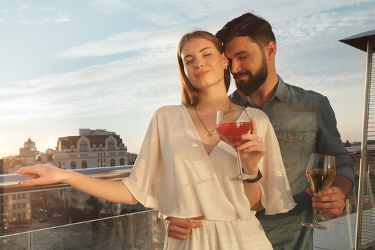 Happy loving couple cuddling on sunset, drinking wine on the balcony