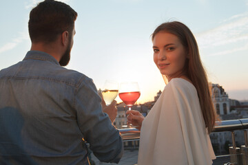 Beautiful woman smiling to the camera enjoying sunset views with her boyfriend at city rooftop bar
