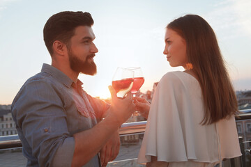 Young couple watching sunset at rooftop bar, drinking wine, celebrating anniversary