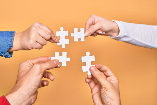 Hands of caucasian young people connecting pieces of puzzle over isolated yellow background