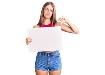 Fototapeta premium Young beautiful blonde woman holding blank empty banner with angry face, negative sign showing dislike with thumbs down, rejection concept