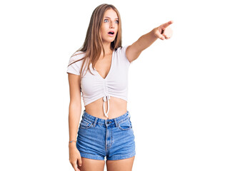 Young beautiful blonde woman wearing casual white tshirt pointing with finger surprised ahead, open mouth amazed expression, something on the front