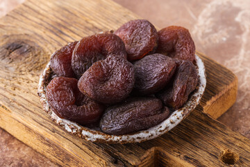 Dried apricots in ceramic plate on wooden board, brown background, healthy concept.