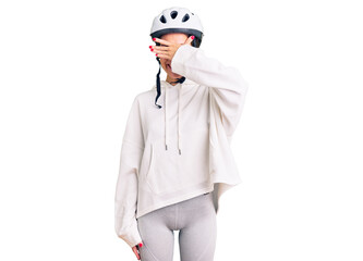 Beautiful brunette young woman wearing bike helmet and sporty clothes smiling and laughing with hand on face covering eyes for surprise. blind concept.