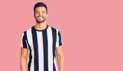 Young handsome hispanic man wearing striped tshirt with a happy and cool smile on face. lucky person.