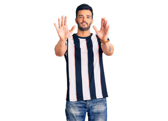 Fototapeta premium Young handsome hispanic man wearing striped tshirt afraid and terrified with fear expression stop gesture with hands, shouting in shock. panic concept.