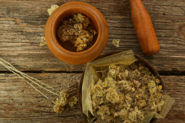 Top view of wooden mortar and pestle and bowl of yellow immortelle flowers on rustic wooden background.