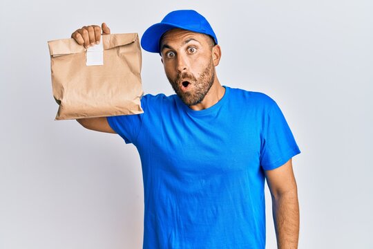 Handsome man with beard holding delivery package scared and amazed with open mouth for surprise, disbelief face