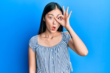 Young chinese woman wearing casual striped t-shirt doing ok gesture shocked with surprised face, eye looking through fingers. unbelieving expression.
