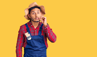 Handsome latin american young man weaing handyman uniform mouth and lips shut as zip with fingers....