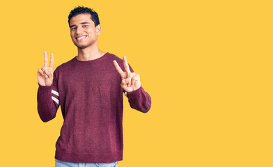Hispanic handsome young man wearing casual clothes smiling looking to the camera showing fingers doing victory sign. number two.