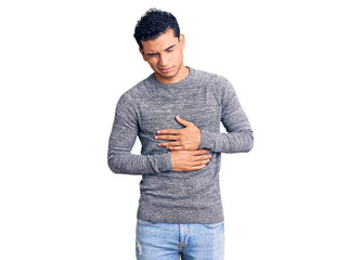 Hispanic handsome young man wearing casual sweater with hand on stomach because indigestion, painful illness feeling unwell. ache concept.