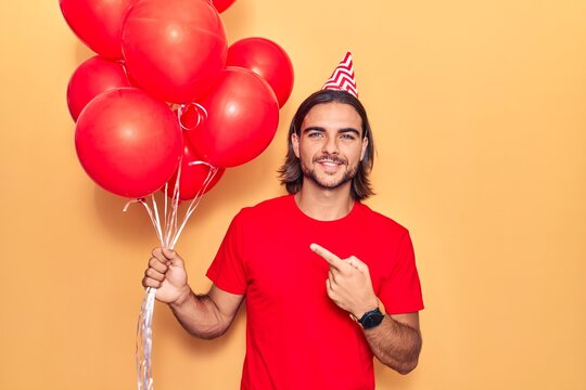 Young handsome man holding balloons smiling happy pointing with hand and finger