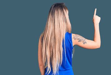 Young beautiful blonde woman wearing cheerleader uniform posing backwards pointing ahead with...