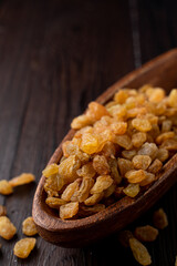 Close up of golden raisins in a wooden bowl, close up, dark background, studio photo with soft light