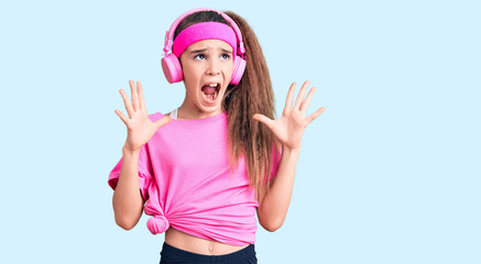 Obraz na płótnie Canvas Cute hispanic child girl wearing gym clothes and using headphones crazy and mad shouting and yelling with aggressive expression and arms raised. frustration concept.