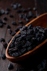 Close up of black raisins in a wooden bowl, close up, dark background, studio photo with soft light