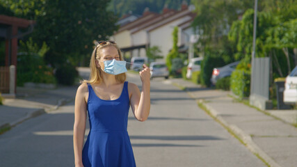 PORTRAIT: Girl standing in the middle of the street takes off her facemask.