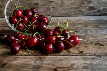 Ripe red cherries in glassware scattered on wooden boards.