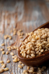 Pine nuts in a wooden bowl on a light rustic wooden table, close up, selective focus, catalogue photo