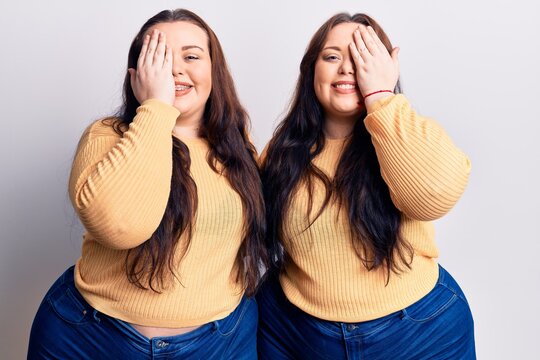 Young plus size twins wearing casual clothes covering one eye with hand, confident smile on face and surprise emotion.