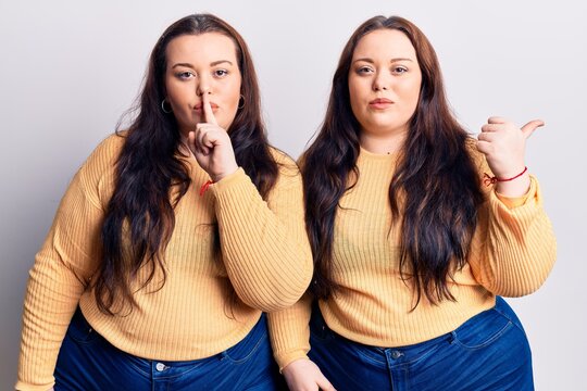 Young plus size twins wearing casual clothes asking to be quiet with finger on lips pointing with hand to the side. silence and secret concept.