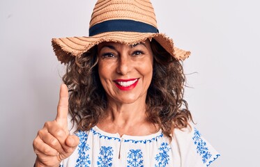 Middle age beautiful brunette woman on vacation wearing summer hat over white background smiling with an idea or question pointing finger up with happy face, number one