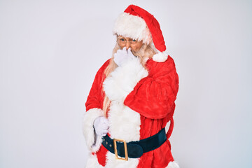 Old senior man with grey hair and long beard wearing santa claus costume with suspenders smelling something stinky and disgusting, intolerable smell, holding breath with fingers on nose. bad smell