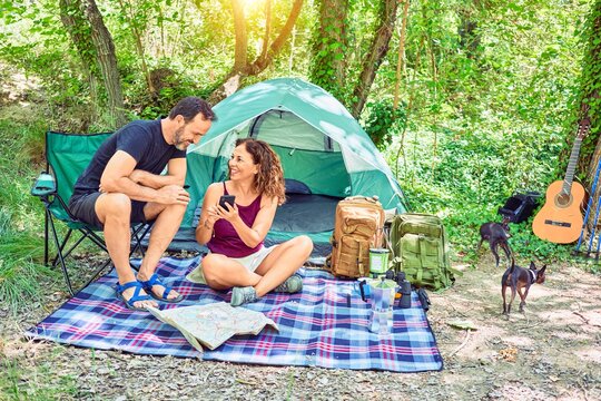 Middle age couple  of hiker smiling happy camping at the forest. Sitting on the floor using smartphone.